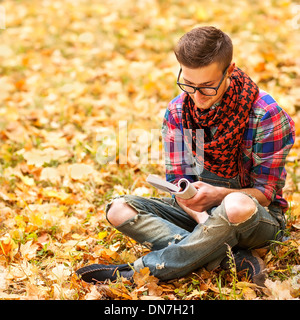 Les jeunes détendue hipster man reading book in nature, retour sur l'arbre, prairie derrière Banque D'Images