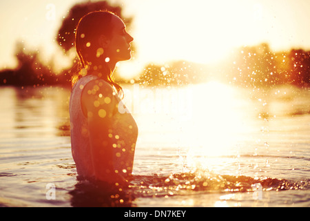 Jeune femme dans un lac au coucher du soleil avec de l'eau éclaboussant Banque D'Images