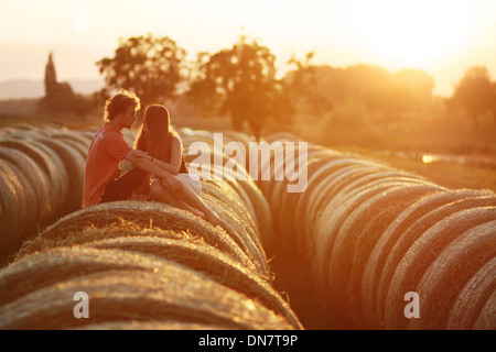 Loving couple sitting on hay bales in backlight Banque D'Images