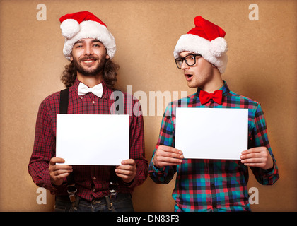 Noël, x-mas, les gens, la publicité, la vente concept - deux heureux homme à Santa helper hat avec tableau blanc vierge. Style hippie. Banque D'Images