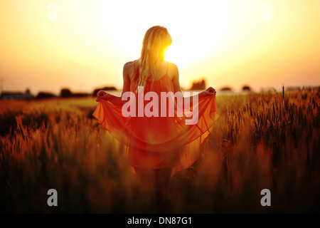 Robe femme debout dans le champ de blé au coucher du soleil Banque D'Images