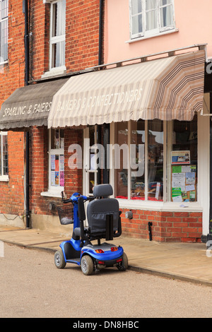 Scooter de mobilité stationné dans un village de l'extérieur de la rue boulanger local dans la boutique, Lavenham Suffolk, East Anglia, Angleterre, Royaume-Uni, Grande Bretagne. Banque D'Images