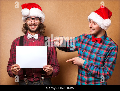 Noël, x-mas, les gens, la publicité, la vente concept - deux heureux homme à Santa helper hat avec tableau blanc vierge. Style hippie. Banque D'Images