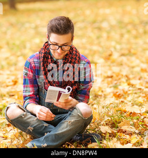 Les jeunes détendue hipster man reading book in nature, retour sur l'arbre, prairie derrière Banque D'Images