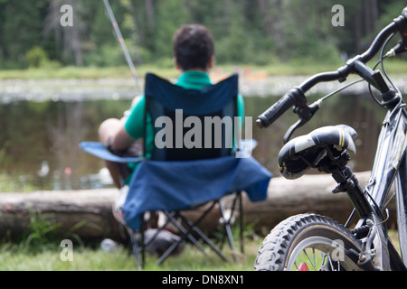 Un adolescent par la pêche dans son campement au bord d'un fauteuil. L'accent sur le vélo. Banque D'Images