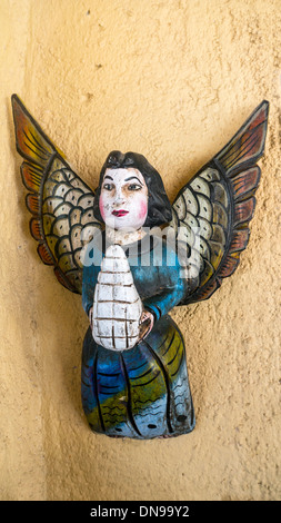 Charmant aux couleurs vives peintes grossièrement l'art populaire mexicain bas-relief d'ange avec des ailes d'or accroché à mur jaune Mexique Banque D'Images