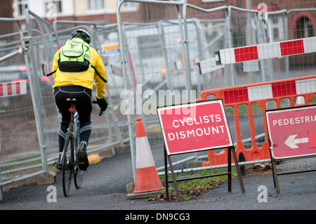 Cycliste sur la chaussée équitation passé cycliste "démonter" signe en travaux Banque D'Images