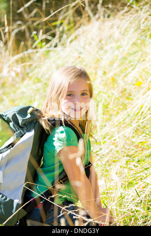 Kid girl blonde explorer la marche avec sac à dos entre l'herbe de la forêt Banque D'Images