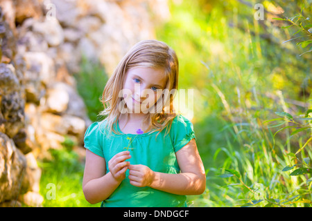 Kid blonde girl smiling avec fleur pourpre détendu en plein air vert Banque D'Images