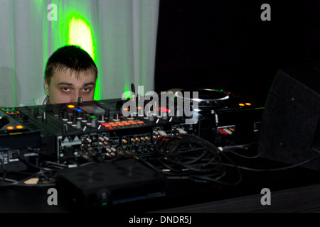 Disc Jockey à son travail qu'il le joue de la musique lors d'une fête avec juste ses yeux visible à la recherche sur le haut de la platine et des commutateurs. Banque D'Images