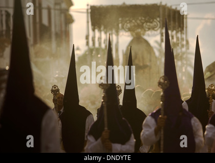 Pénitents marcher devant un trône de l'affichage d'une sculpture de Notre Dame des Douleurs durant Pâques Semaine Sainte procession en Carmona Banque D'Images