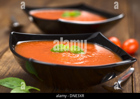 Soupe de tomates fraîches faites maison avec des feuilles de basilic sur le dessus servi dans un bol en bois foncé sur noir Banque D'Images