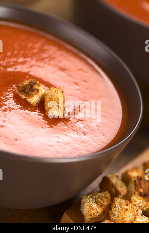 Soupe de tomates fraîches faites maison avec croûtons de farine sur le dessus en bois sombre sur bol brun Banque D'Images