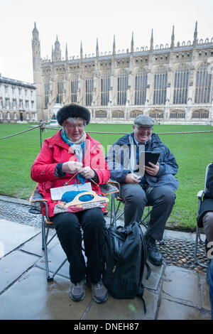 Cambridge, UK. Le 24 décembre, 2013. Une dame tricote et un homme lit un livre tout en file d'elles pour le Festival de neuf leçons et Noël au King's College de Cambridge, au Royaume-Uni, juste après l'aube du 24 décembre 2013. Certains dormaient la nuit, bravant la pluie et le vent qui a balayé le pays pour obtenir une bonne place dans la file d'attente. Le traditionnel concert de Noël a lieu au plus tard la veille de Noël et est diffusé dans le monde entier. Julian crédit Eales/Alamy Live News Banque D'Images