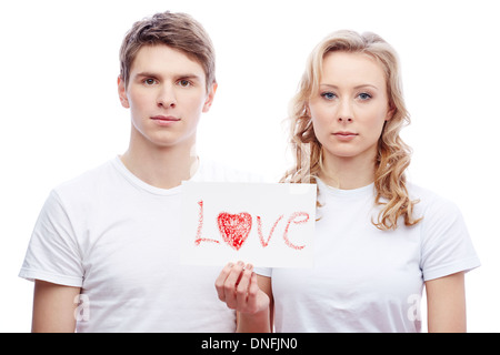 Portrait of young couple looking at camera while girl holding paper avec mot amour Banque D'Images