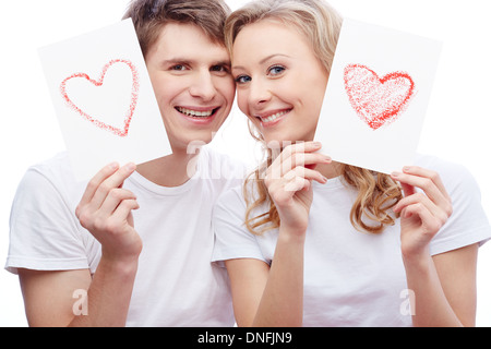 Portrait of young amorous couple looking at camera tout en maintenant les papiers avec des coeurs Banque D'Images