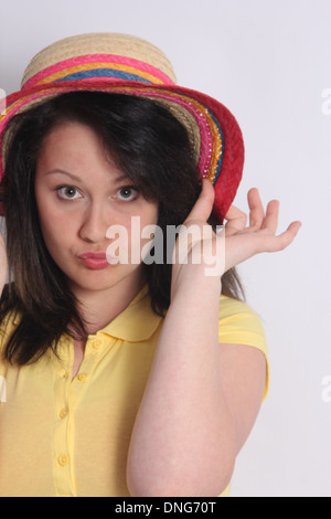 Jeune fille brune jouant avec un chapeau de paille sur sa tête. Banque D'Images