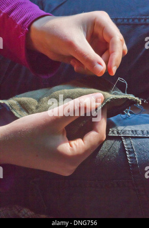 Close up of young female hands la couture d'un morceau de tissu avec aiguille et fil Banque D'Images