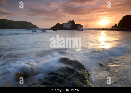 La marée s'engouffre dans sur les roches dans le port de Hope Cove, Devon, Angleterre, au coucher du soleil. Banque D'Images