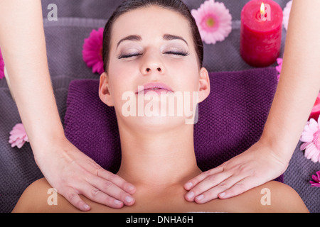 Close-up portrait de dessus d'une jeune femme brune attrayante ayant un massage facial relaxant, dans un centre spa de fantaisie, avec des bougies parfumées et des fleurs Banque D'Images