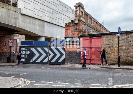 Deux jeunes hommes à roulettes et vieille brique mur dans Brick Lane, Londres E1 Banque D'Images