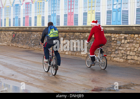 Santa et ami à cheval le long du front de mer de Bournemouth sur leurs vélos dernière peinture de l'cabines de plage le jour de Noël Banque D'Images