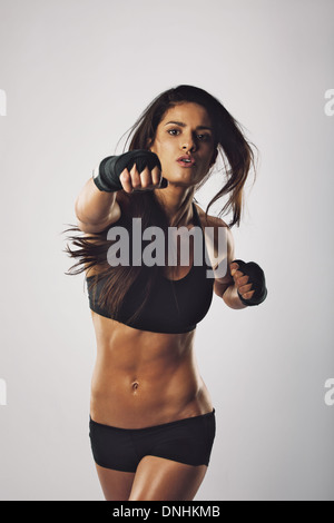 Jeune femme monter vers la caméra de poing contre l'arrière-plan gris. Middle Eastern female boxer pratiquer la boxe. Banque D'Images