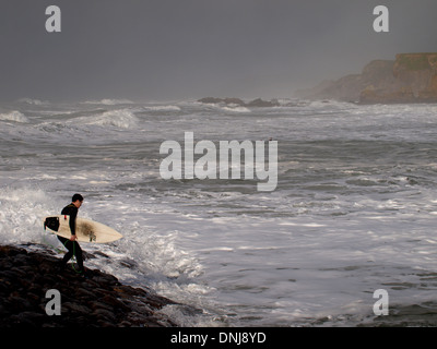 Surfer se déversant dans la mer des rochers en hiver, Bude, Cornwall, UK Banque D'Images