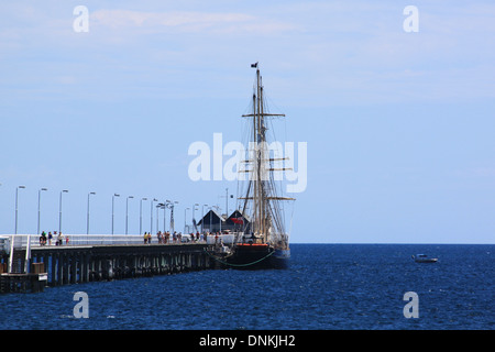 Une photographie de Busselton Pier (jetée) près de Perth en Australie de l'Ouest avec un grand voilier amarré contre elle. Banque D'Images