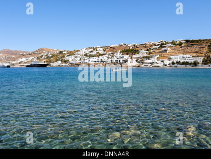 Avis de sunny Chora, Mykonos, Grèce port avec ciel bleu clair, un bateau de pêche et de plaisance ; pierres visibles dans l'eau peu profonde Banque D'Images