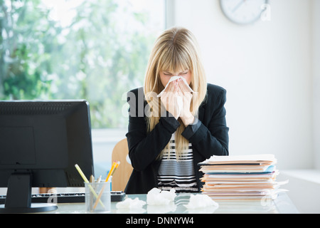 Man blowing nose in office Banque D'Images
