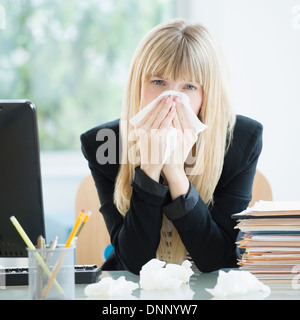 Man blowing nose in office Banque D'Images