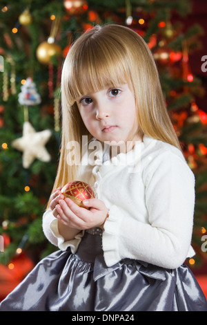 Une fillette de trois ans avec un arbre de Noël derrière elle Banque D'Images