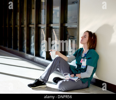 Épuisé infirmière assise sur le sol avec les yeux fermés tenant une tasse en styromousse Banque D'Images