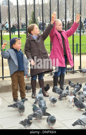 Deux jeunes filles et un jeune garçon se nourrir les moineaux et les pigeons dans une rue de Paris, France Banque D'Images