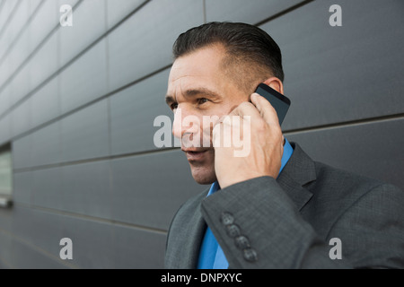 Close-up portrait of businessman standing in front of mur du bâtiment à l'aide d'un téléphone cellulaire, Mannheim, Allemagne Banque D'Images