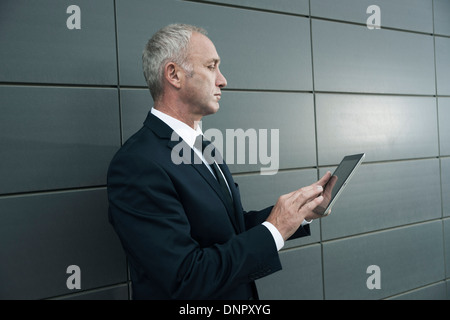 Businessman standing in front of wall, looking at tablet computer Banque D'Images