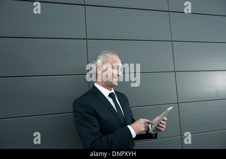 Businessman standing in front of wall, looking at tablet computer Banque D'Images