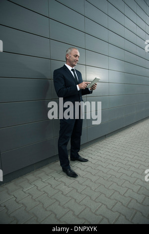 Businessman standing in front of wall, looking at tablet computer Banque D'Images