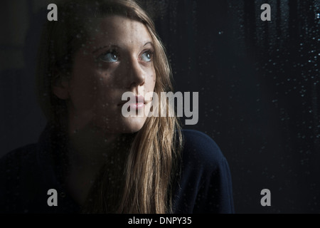 Portrait de jeune femme derrière fenêtre, humide avec des gouttes de pluie, jusqu'à Banque D'Images