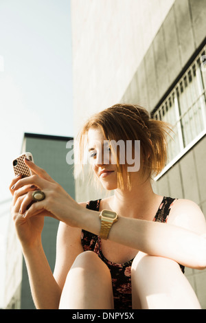 Teenage girl sitting outdoors et looking at smartphone Banque D'Images