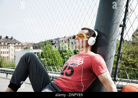 Man sitting on outdoor basketball portant des écouteurs et écouter de la musique, de l'Allemagne Banque D'Images