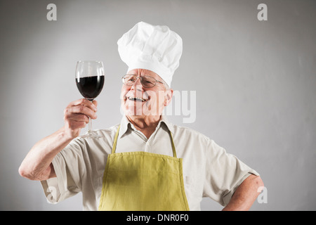 Senior Man with Red Wine portant Tablier et chapeau de chef, Studio Shot Banque D'Images