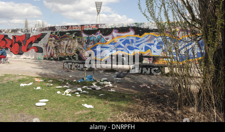 Portée sur l'herbe en face de la Mur de Berlin (Hinterlandmauer) avec graffiti bleu et rouge scrawl, Mauerpark, Berlin, Allemagne Banque D'Images