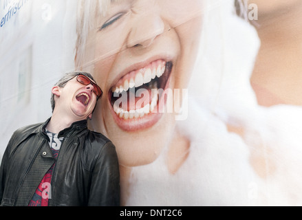 Jeune homme portant la copie de l'affiche des tons billboard femme en riant la bouche grande ouverte et les yeux fermés Banque D'Images