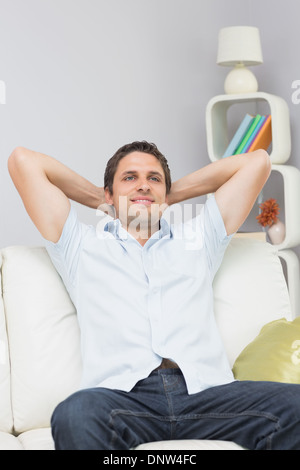 Thoughtful homme assis avec les mains derrière la tête dans la salle de séjour Banque D'Images