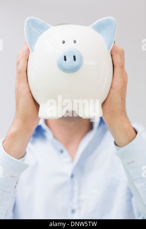 Casual man holding piggy bank en face de son visage Banque D'Images