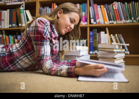 Smiling student lying on library floor reading Banque D'Images