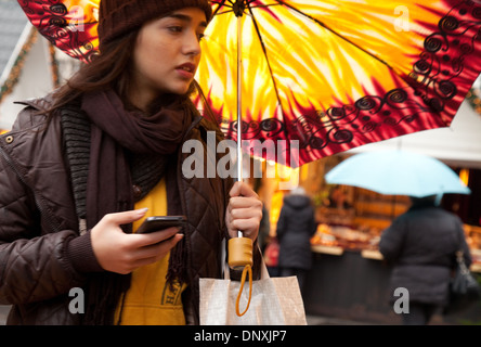 Anxieux attractive young woman in a rush, les sms sur un téléphone mobile, et tenant un parapluie coloré, Cologne, Allemagne l'Europe Banque D'Images