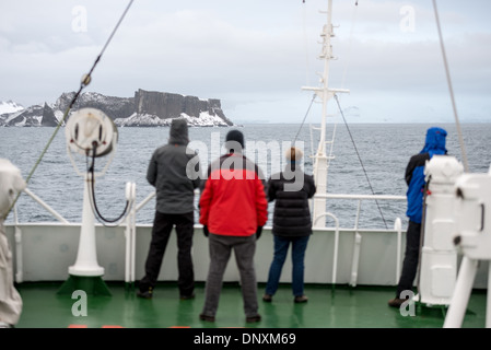 L'ANTARCTIQUE - un petit groupe de passagers se tient sur le pont d'un navire de croisière antarctique pour voir les premières terres aperçues après passage de Drake. L'île dans la distance fait partie des îles Shetland du Sud le long du détroit de l'anglais et l'Île Robert juste à côté de la péninsule antarctique. Banque D'Images